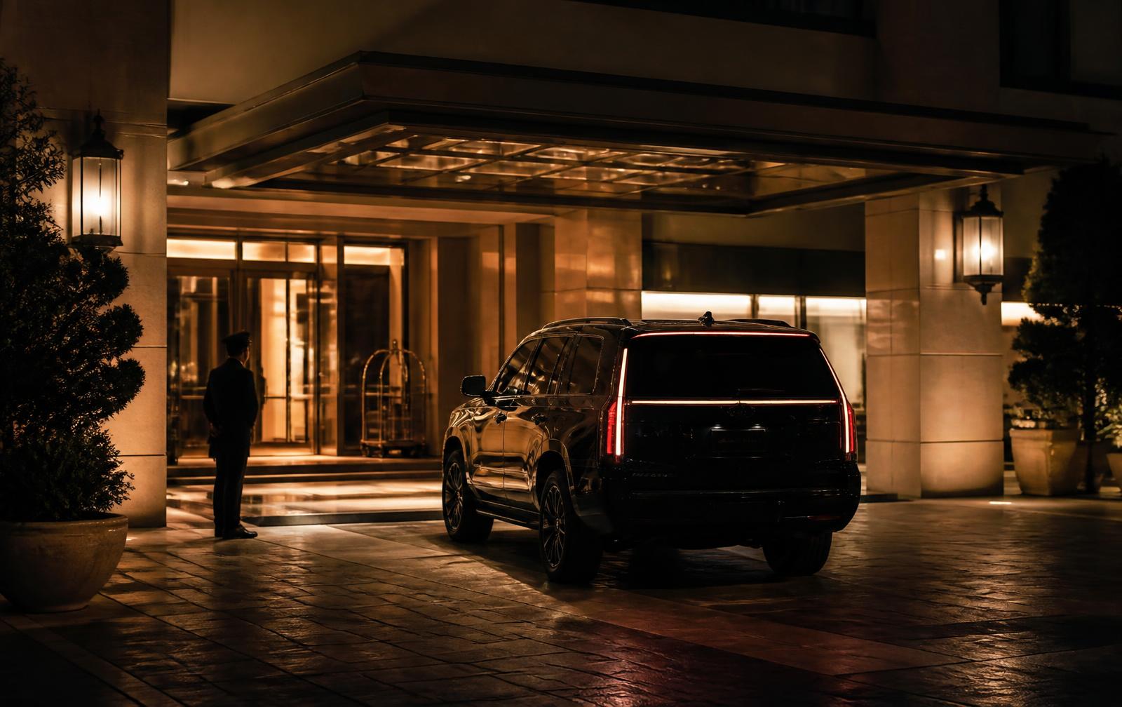 Black luxury SUV arriving under the covered entrance of an upscale hotel at night
