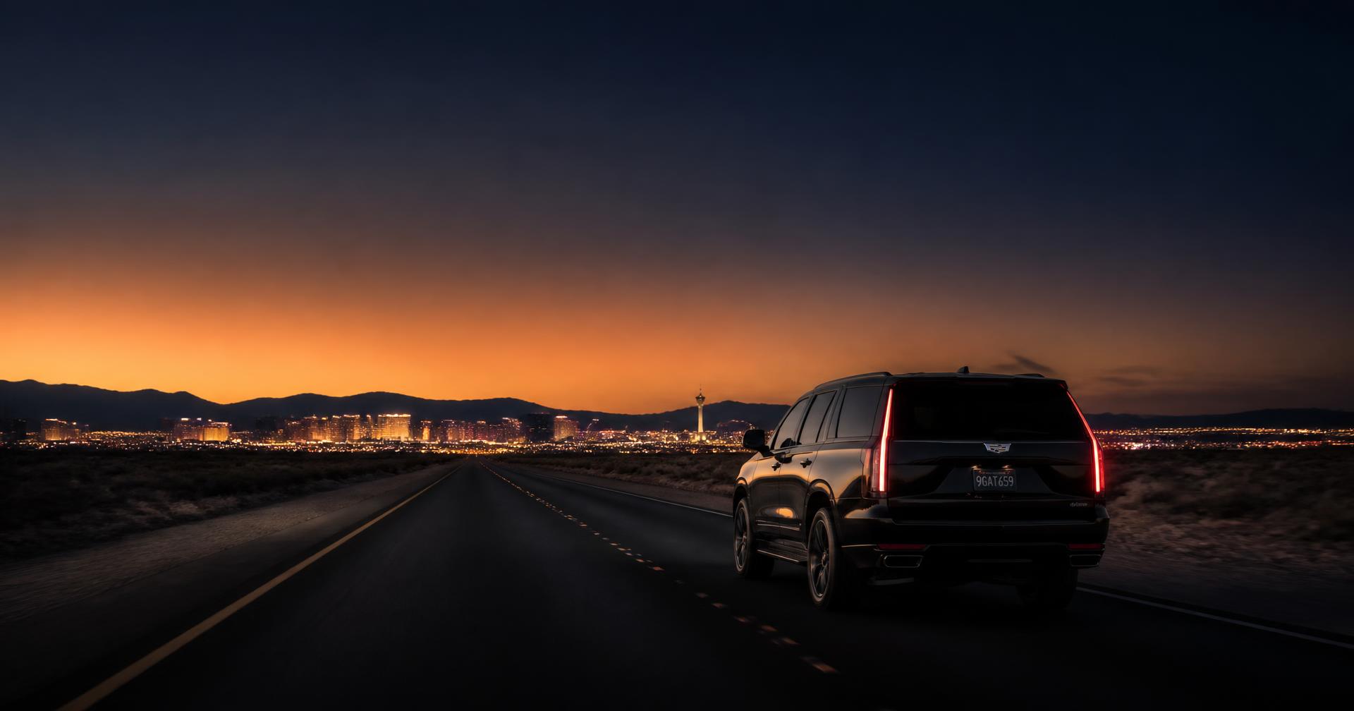 Black luxury SUV on an open highway heading toward the Las Vegas skyline at dusk